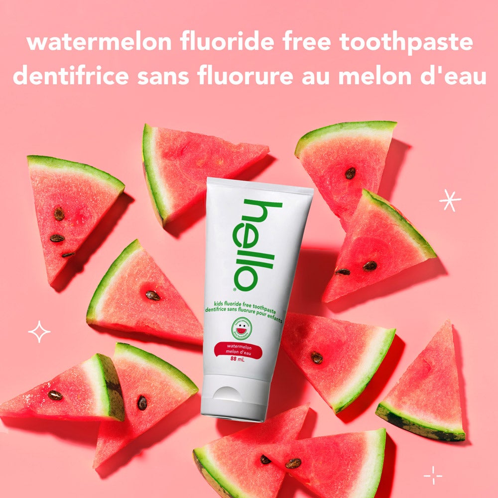 A hand holds a tube of Hello watermelon fluoride-free toothpaste against a pink background. White text beside the product says, &quot;tastes awesome, works brilliantly. removes plaque*. polishes + brightens.&quot; At the bottom, there is a small note: &quot;*with daily brushing.&quot;