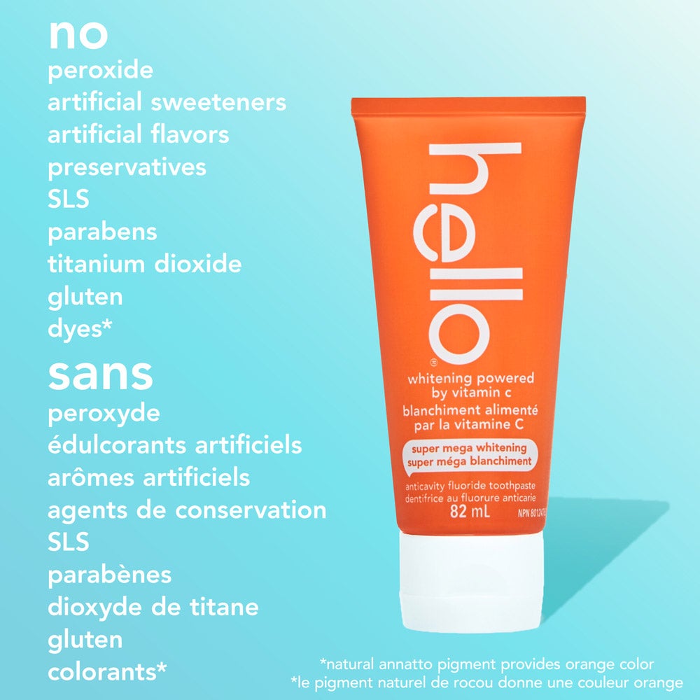 An orange tube of hello super mega whitening toothpaste powered by vitamin C stands upright on a blue background. Text to the left of the tube lists ingredients not included in the product—no peroxide, artificial sweeteners, artificial flavors, preservatives, SLS, parabens, titanium dioxide, gluten, or dyes—with the same information repeated in French. Small text at the bottom notes that the natural annatto pigment provides the orange color in both English and French.