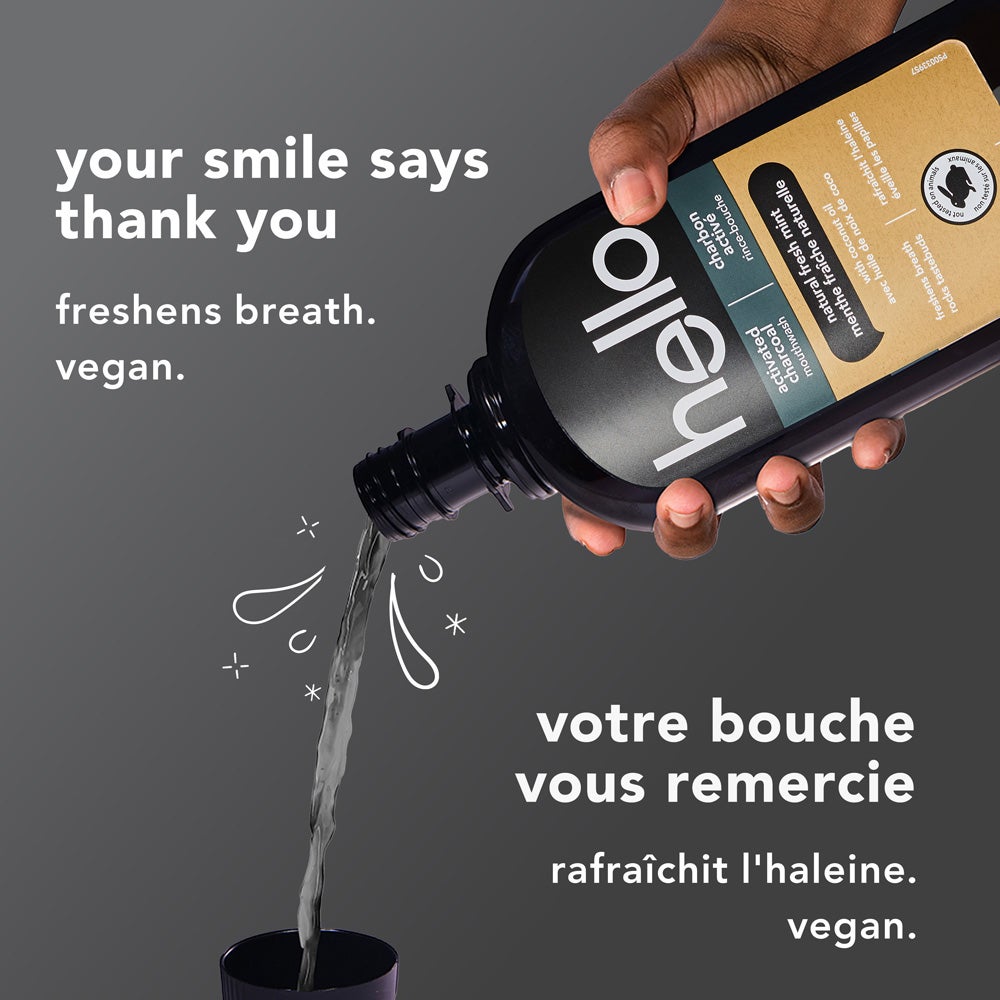 A close-up of a hand pouring hello brand activated charcoal mouthwash into a cup against a gray background. White text says "your smile says thank you – freshens breath. vegan." in English and the French translation below. The product bottle label is visible.